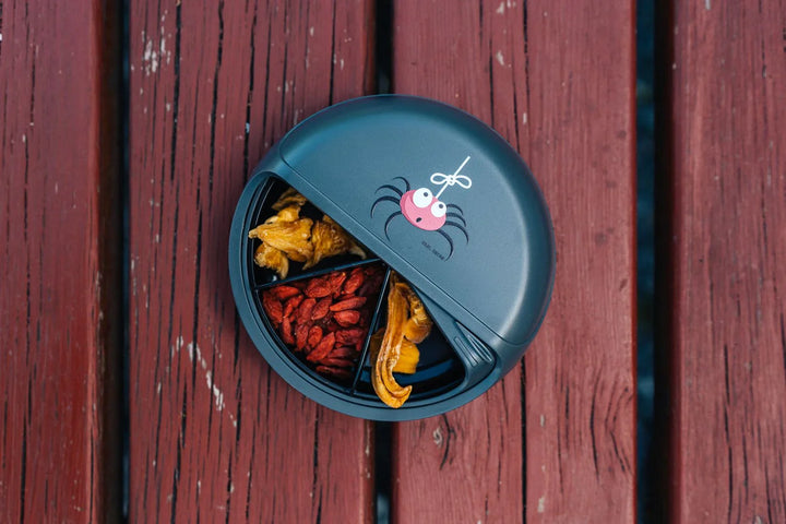 Runde Snackbox mit Spinnendesign, gefüllt mit Trockenfrüchten, auf Holztisch