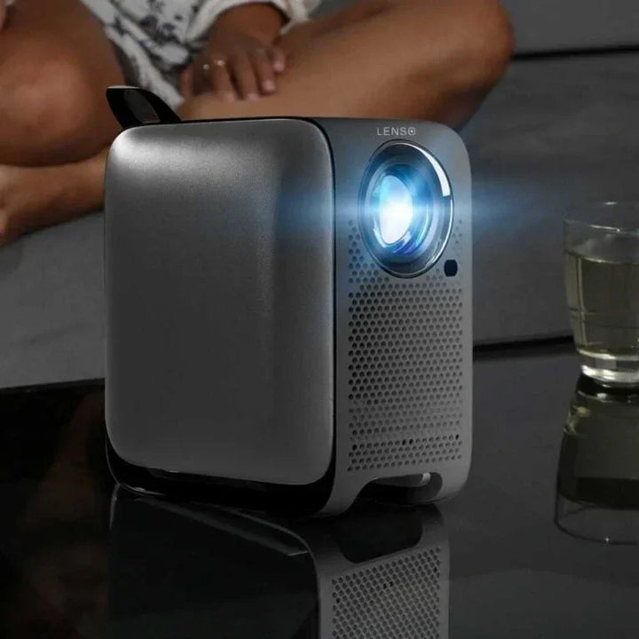 Lenso tragbarer Beamer projiziert Licht im Wohnzimmer neben Glas und Sofa