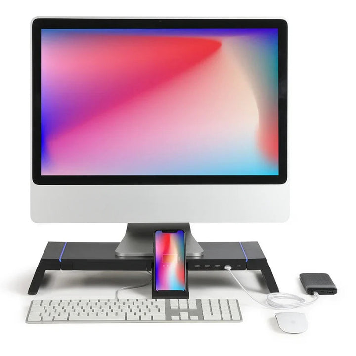 Ein elegantes Desktop-Setup mit einem großen Monitor, einer Tastatur, einer Maus, einem auf einem Ständer aufladbaren Telefon und einer externen Festplatte.