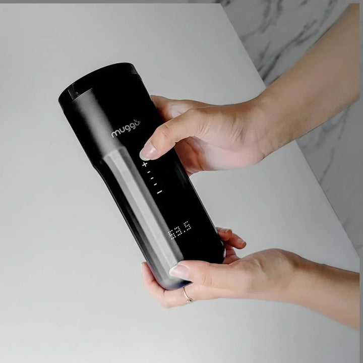 Schwarzer Muggo Thermobecher mit LED-Anzeige, von Hand gehalten auf hellem Tisch.