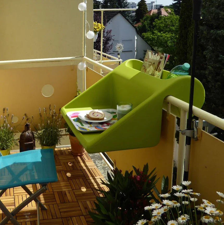 Auf einem hellgrünen Balkontisch stehen ein Getränk und ein Teller mit Dessert, umgeben von Pflanzen und einer sonnigen, fröhlichen Atmosphäre.