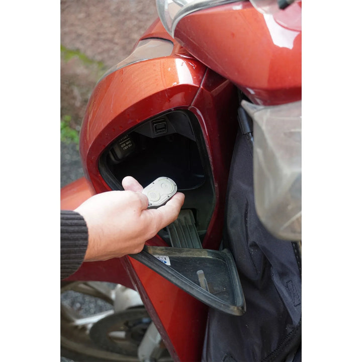Person hält GPS Tracker in das Handschuhfach eines roten Mopeds