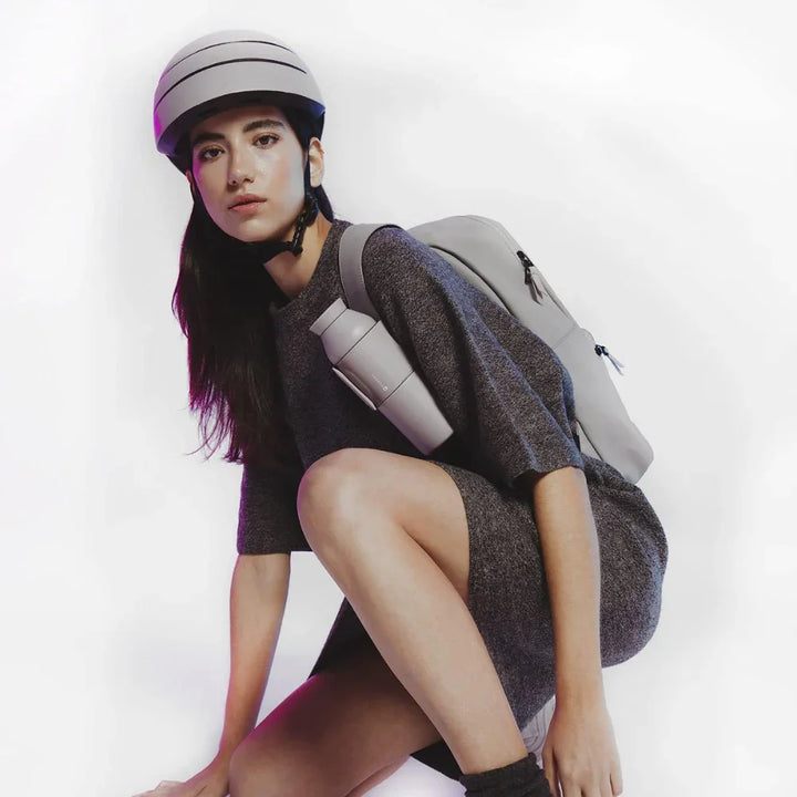 Frau mit faltbarem Fahrradhelm und Trinkflasche am grauen Rucksack, modernes Design