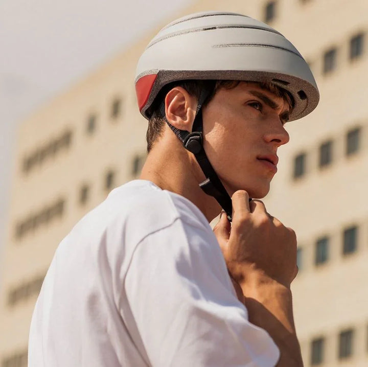 Junger Mann mit weißem Fahrradhelm Closca Urban Fit vor modernem Gebäude im Freien