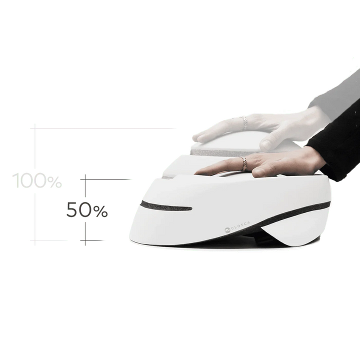 Faltbarer weißer Closca Fahrradhelm, Hände drücken zur Komprimierung, 50% Platzersparnis.