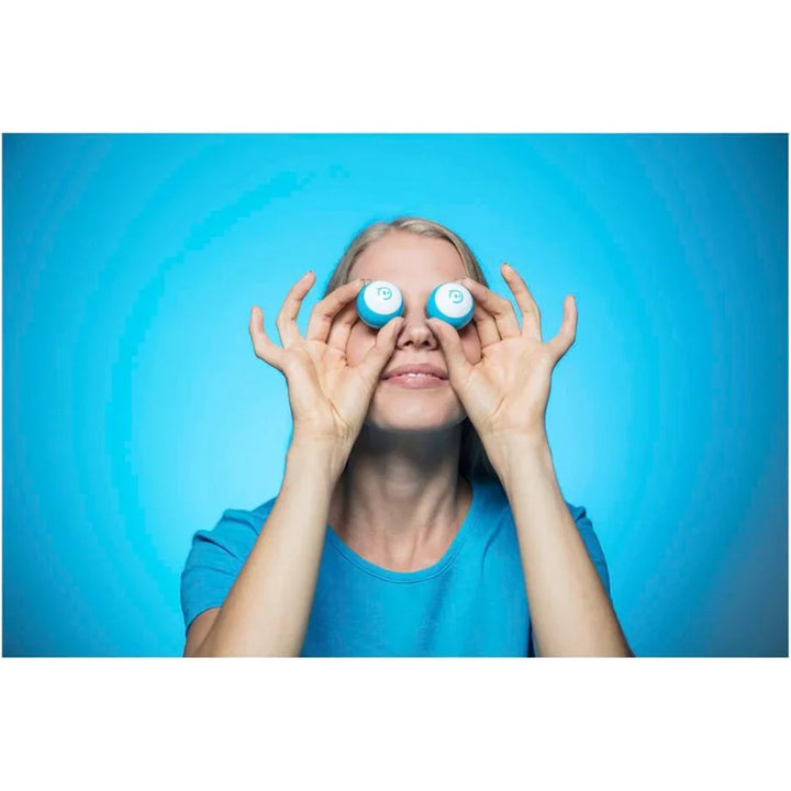 Frau mit blauer Kleidung hält Kontaktlinsenbehälter vor die Augen, blauer Hintergrund