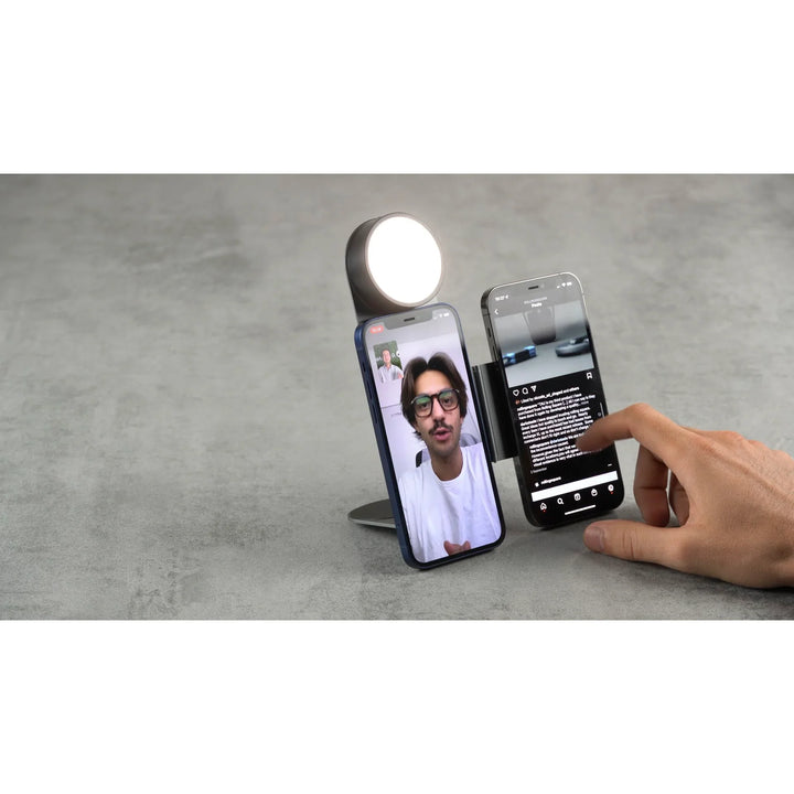 Hand hält zwei Smartphones auf Dual-Handyhalterung mit LED-Licht auf grauer Oberfläche