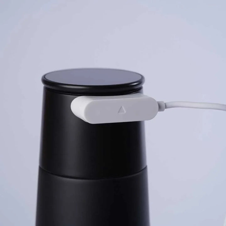 Schwarzer Thermobecher mit weißem Magnetladekabel, minimalistisch, auf hellem Hintergrund