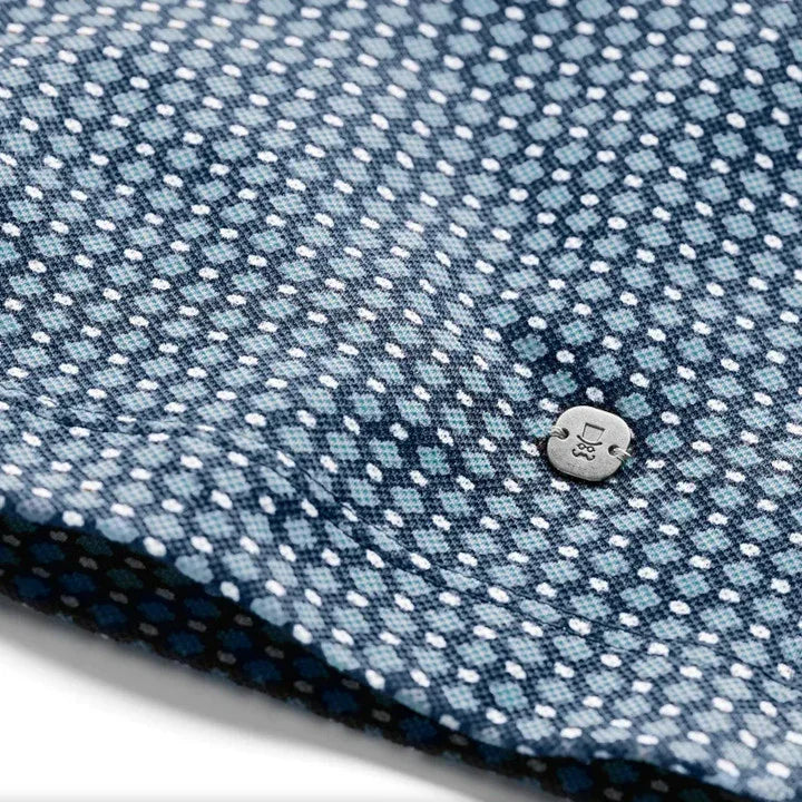 Detailaufnahme blaues Poloshirt mit weißem Punktmuster und silbernem Logo-Button