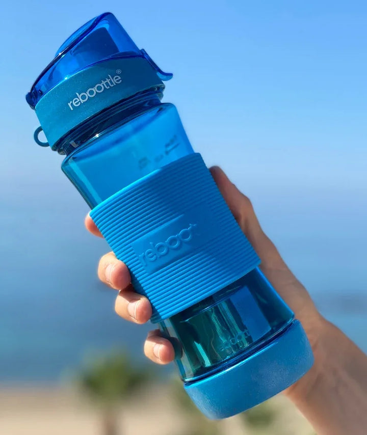 Blaue rebottle Trinkflasche aus Glas wird draußen in einer Hand gehalten vor blauem Himmel.