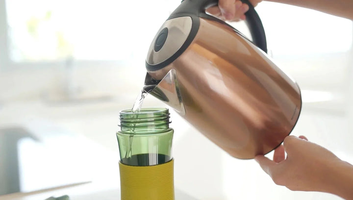 Wasser wird aus Kupferkessel in grüne Teeflasche auf Arbeitsplatte gegossen