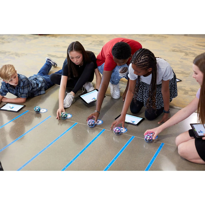 Kinder steuern Sphero Lernroboter mit Tablets auf dem Boden im Klassenzimmer.