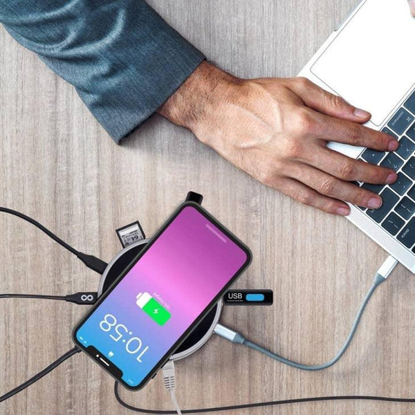 Mann arbeitet am Laptop, Smartphone lädt auf Wireless-Ladestation mit USB-Hub auf Schreibtisch