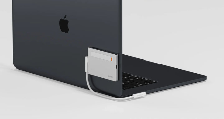 Eine elegante silberne Powerbank, die an der Rückseite eines schwarzen Laptops angebracht ist, wobei das Ladekabel zum USB-C-Anschluss des Laptops führt.
