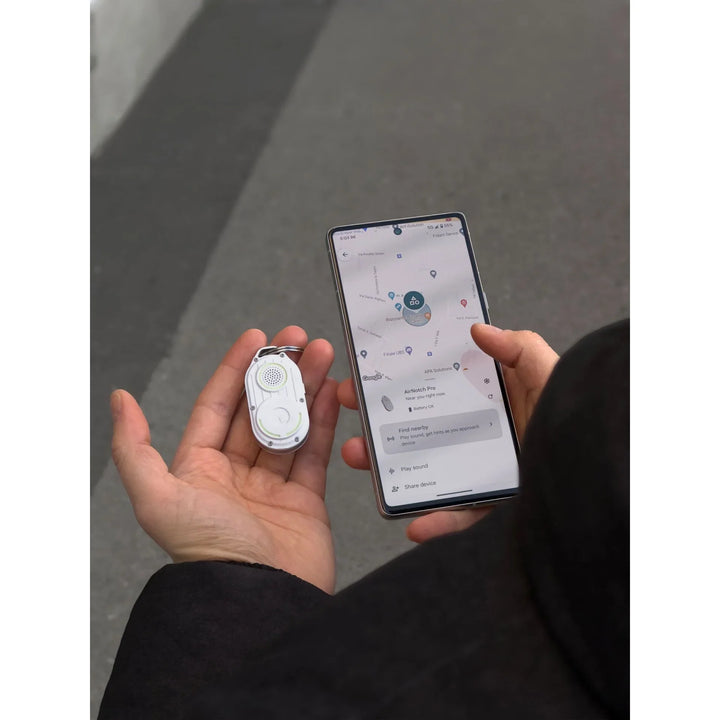 Hand hält weißen AirNotch Tracker und Smartphone mit Find My App auf grauem Hintergrund