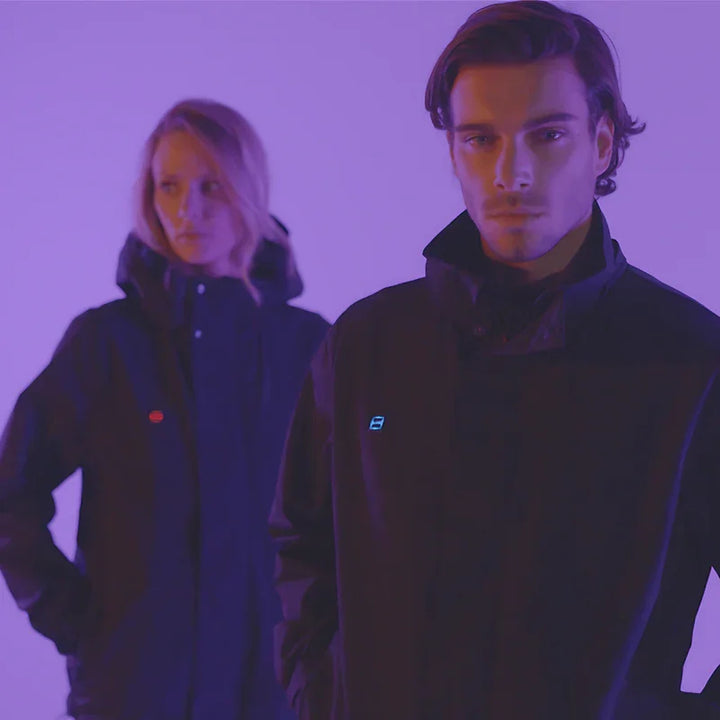 Zwei Personen tragen schwarze Allwetter-Jacke unter lila Beleuchtung, moderne Outdoor-Mode.