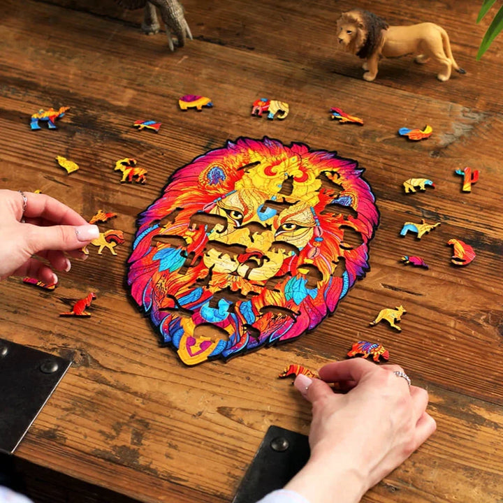 Ein buntes Löwenpuzzle, umgeben von verstreuten Teilen, wobei eine Person das letzte Teil auf einen Holztisch legt.