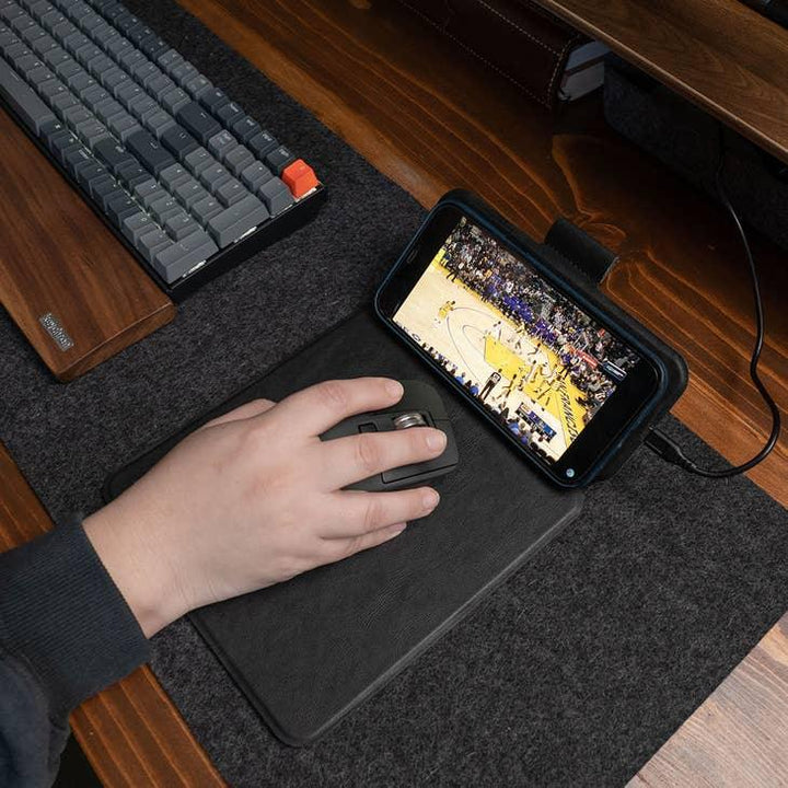 Hand mit Computermaus auf Mauspad vor Tastatur, Smartphone zeigt Basketballspiel